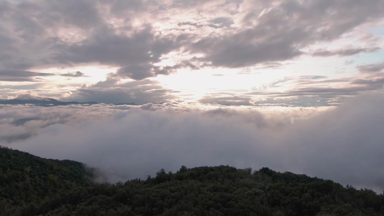 Drone flying above tall mountain near clouds during beautiful sunset
