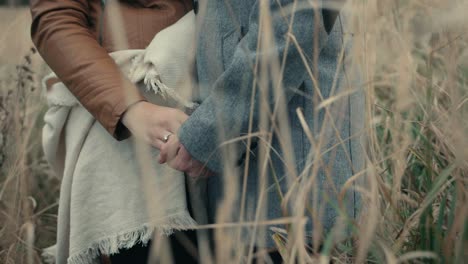 Couple-holding-hands-standing-close-to-each-other,-in-a-field-with-tall-grass