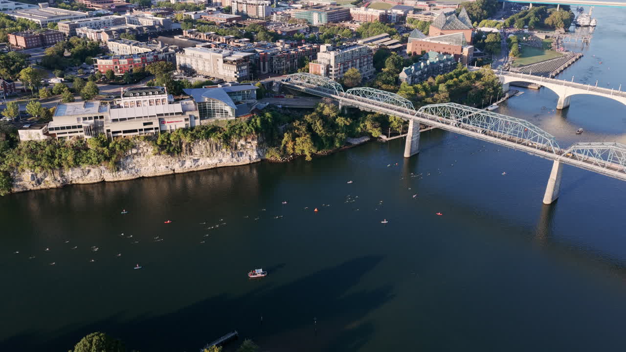Athletes swim along the Tennessee River beneath Chattanooga’s bluffs, guided by kayakers near the historic bridges and downtown skyline
