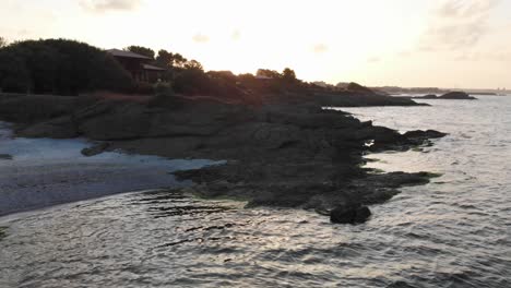 Aerial-panning-shot-around-houses-on-rocky-seashore-at-sunset