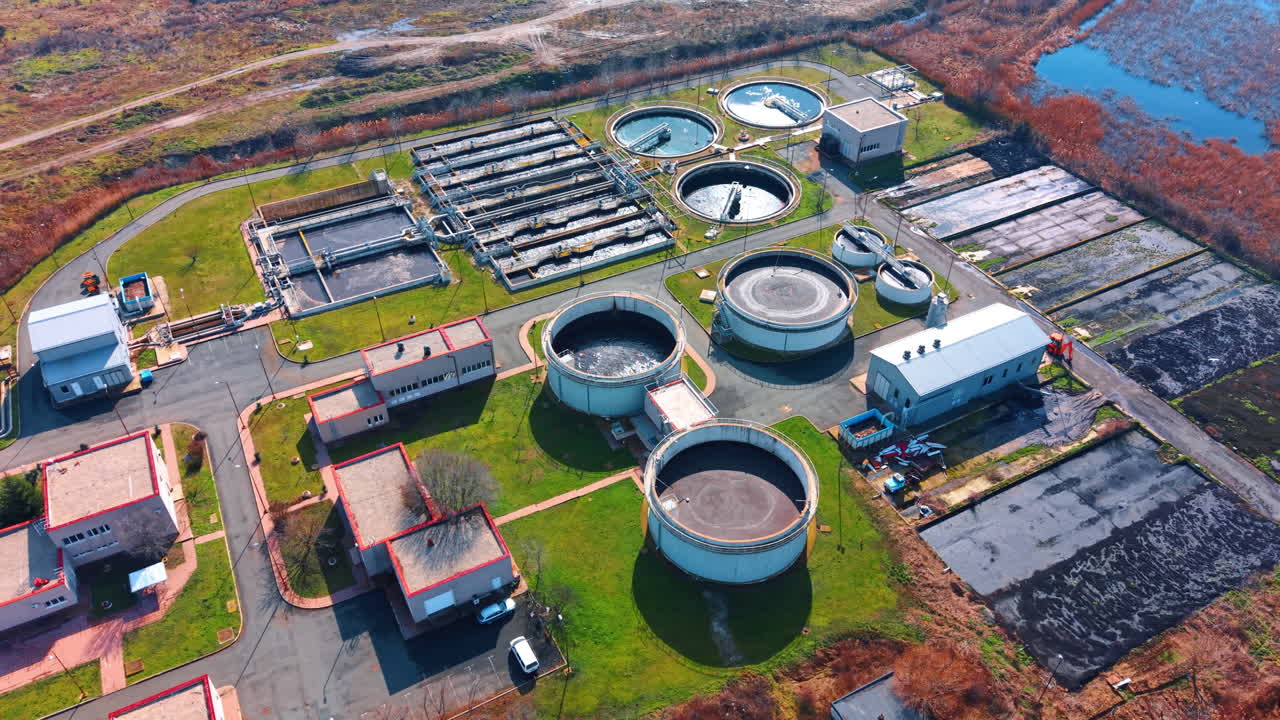 High angle view of water purification facility with wetlands background. Industrial complex featuring circular settling tanks and service buildings at sunset light