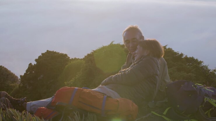 Pareja mayor tumbada en la montaña, besándose y disfrutando de la vista.