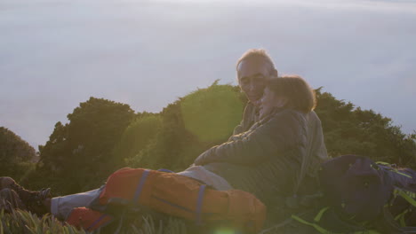 pareja mayor tumbada en la montaña, besándose y disfrutando de la vista