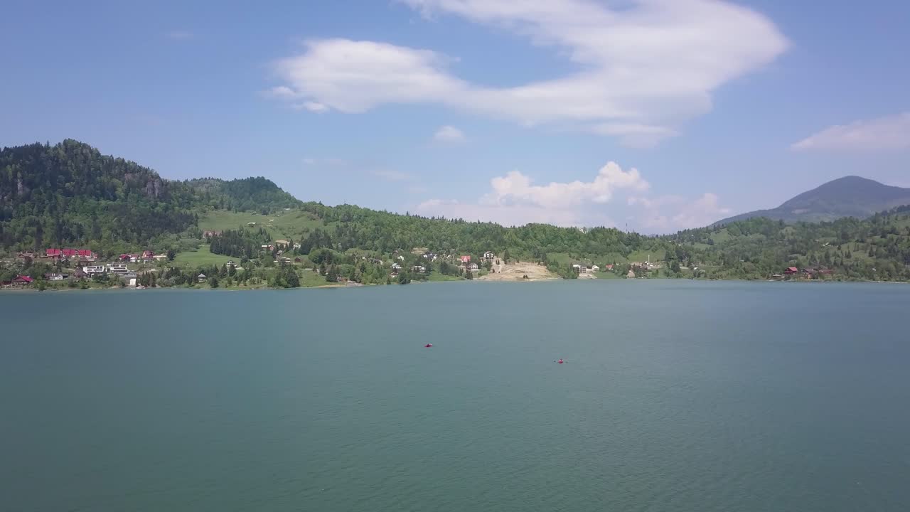 배경 에 산 들 과 파란 하늘 을 가로질러 부분적 인 구름 이 있는 호수 의 공중  촬영