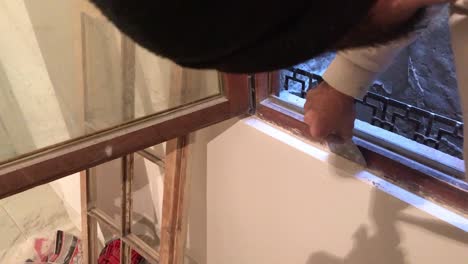 young man removing excess of plaster with scraper around wooden window frame in 4k