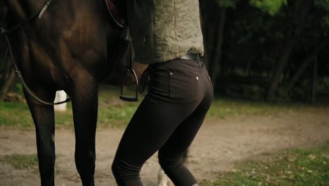 Close-Up-view-of-unrecognizable-professional-horse-rider-dismounting-from-the-horse,-jumping-on-the-ground