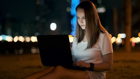 Eine-Softwareentwicklerin-Sitzt-An-Einem-Sommerabend-In-Einem-Park-In-Der-Stadt-Und-Schreibt-Code,-Während-Sie-Auf-Einen-Laptop-Bildschirm-Schaut.-Drucken-Sie-Den-Artikel-Auf-Einem-Laptop-Aus.-Der-Blogger-Antwortet-Auf-Beiträge