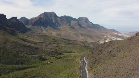 Panorama-drone-shot-of-a-car-driving-through-a-canyon-with-mountains