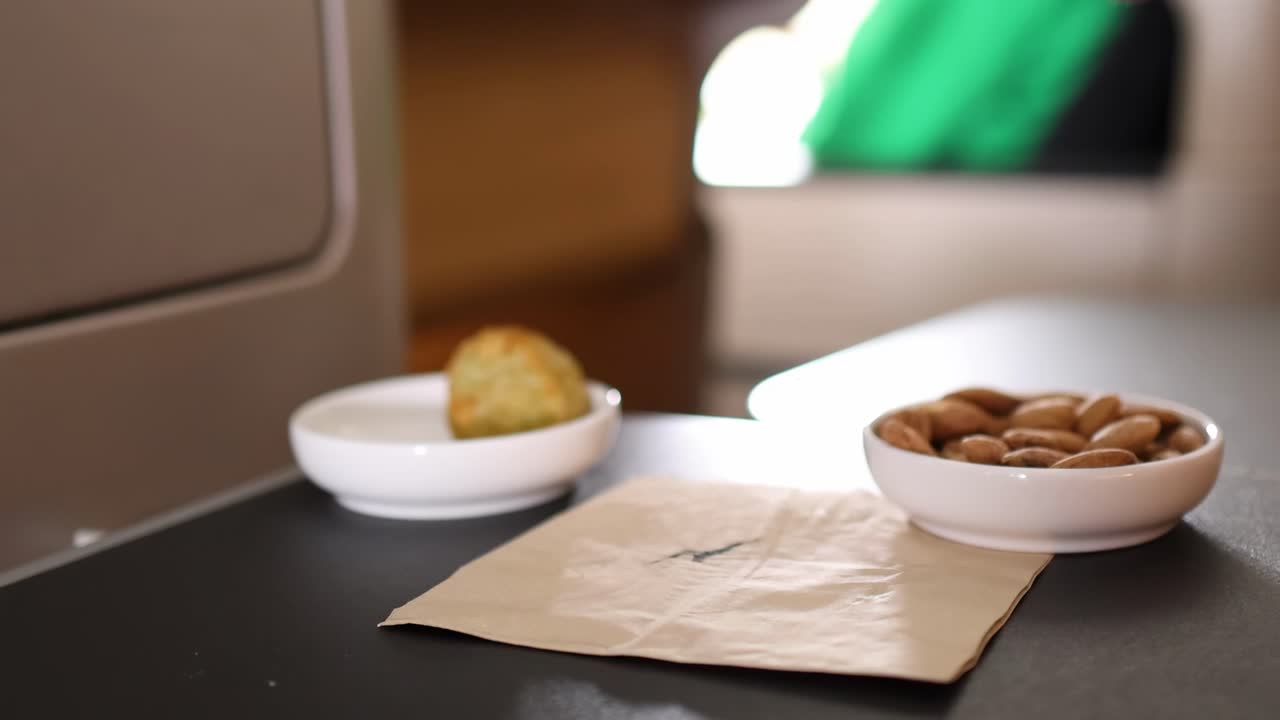 A hand interacts with a glass of red wine and a bowl of almonds on a tray table.