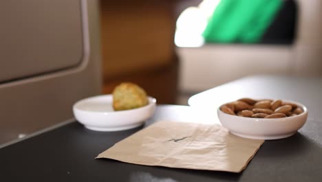 a hand interacts with a glass of red wine and a bowl of almonds on a tray table.