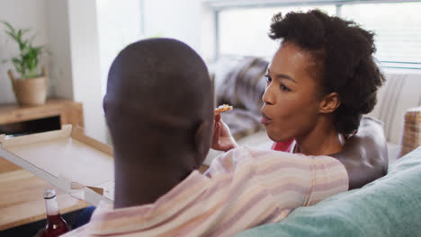 Video-of-back-view-of-african-american-couple-sitting-on-sofa-with-beer-and-talking