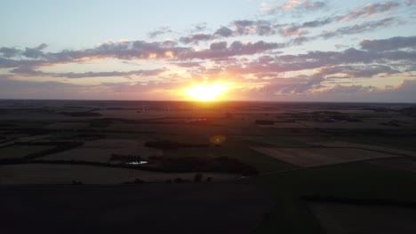 Drohne-Fliegt-Vom-Sonnenuntergang-Weg,-Mit-üppiger-Grüner-Landwirtschaftslandschaft-Auf-Dem-Boden,-In-Dänemark