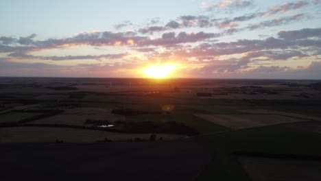 drone vliegt weg van zonsondergang, met weelderig groen boerenlandschap op de grond, in denemarken