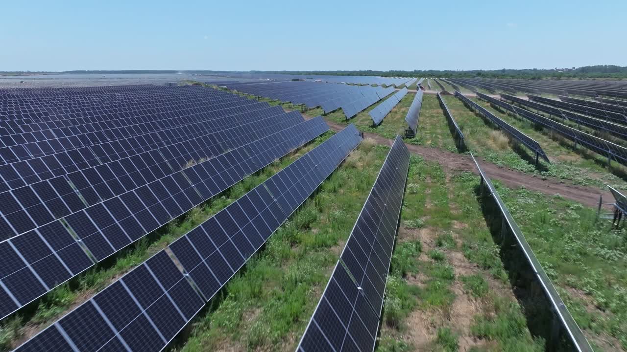 Drone view of vast solar panels in open field, clear sky, sustainable energy
