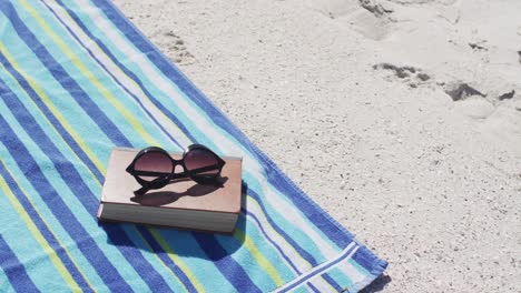 video of sunglasses, book, towels and beach equipment lying on beach