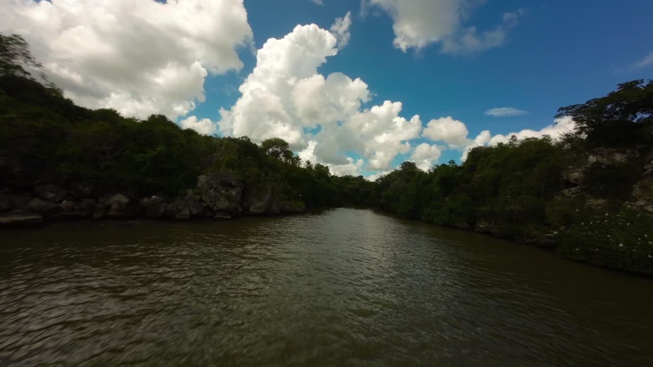 Voo de drone FPV subindo o rio Yuma, com selva verde exuberante nas margens em Boca de Yuma, República Dominicana. Avanço aéreo.