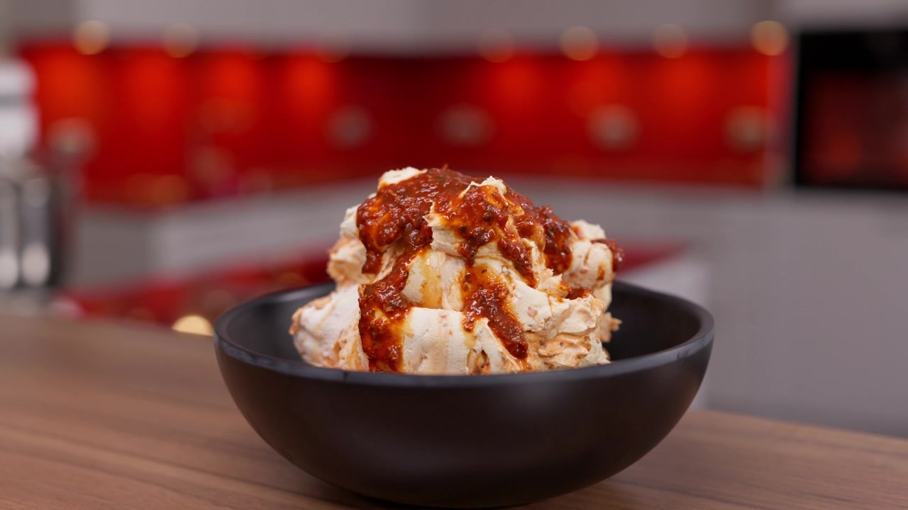 Piatto cremoso e saporito condito con una ricca salsa rossa e servito in una ciotola nera. Ideale per ristoranti, catering, servizi di ristorazione e concetti culinari, primo piano.