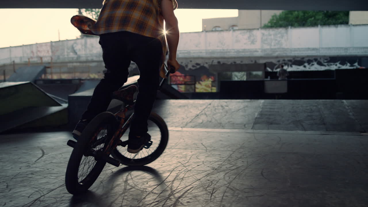 Teenager BMX-rytter udfører springstunt mod en baggrund af klar sol i skateparken.