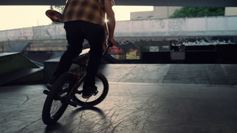 teenage bmx rider performing jump stunt at bright sun background in skate park.