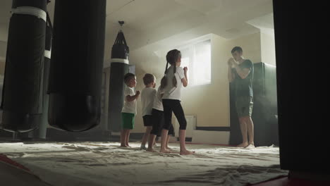 kids do kicks with instructor in karate school. little children train leg fighting techniques with young trainer in gym slow motion. martial arts