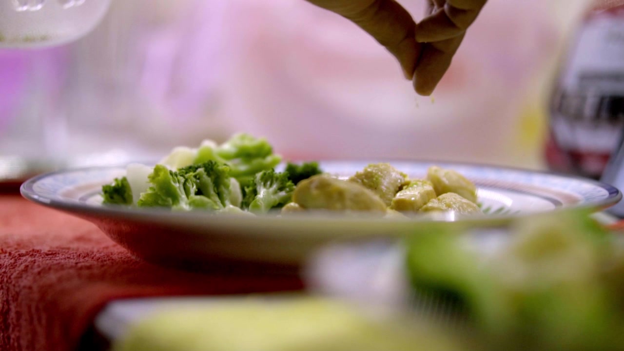 Mano che spreme limone fresco su pollo alla griglia servito con broccoli su un piatto, aggiungendo sapore di agrumi prima di gustare un pasto fatto in casa nella cucina tradizionale messicana.