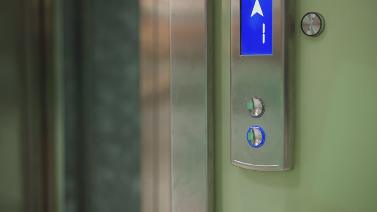 Close-up shot of elevator control panel with illuminated blue arrow pointing upwards, indicating movement to higher floor. Clean modern elevator design with metallic and green walls