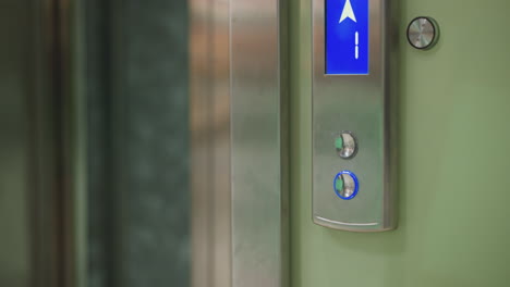 close-up shot of elevator control panel with illuminated blue arrow pointing upwards, indicating movement to higher floor. clean modern elevator design with metallic and green walls