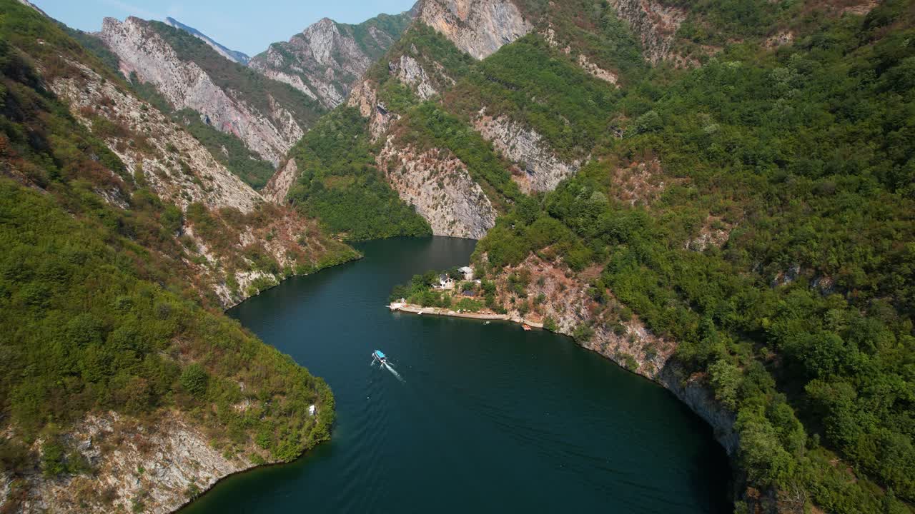 초록색으로 인 높은 바위 산들이 조용한 코만 호수 물에 반사되어 관광객들이 배를 타고 탐험합니다.
