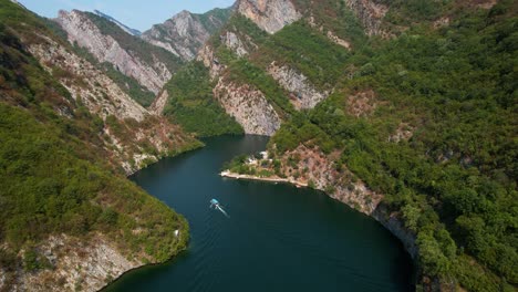 altas montañas rocosas cubiertas de verde se reflejan en las tranquilas aguas del lago koman, los turistas exploran en barco
