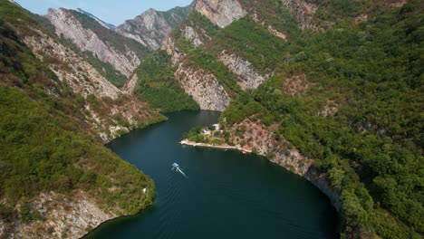 high rocky mountains covered in green reflected in calm koman lake waters, tourists explore by boat