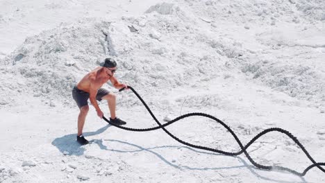 sports activities with ropes on the street. male athlete on the white sand does exercises with a rope