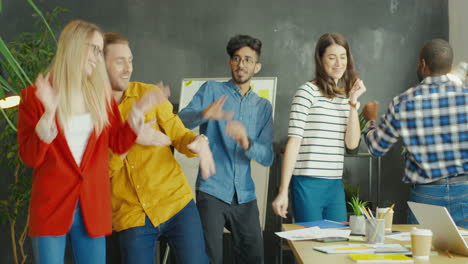 young multicultural entrepreneurs group cheering, dancing and having fun in the office after reaching success