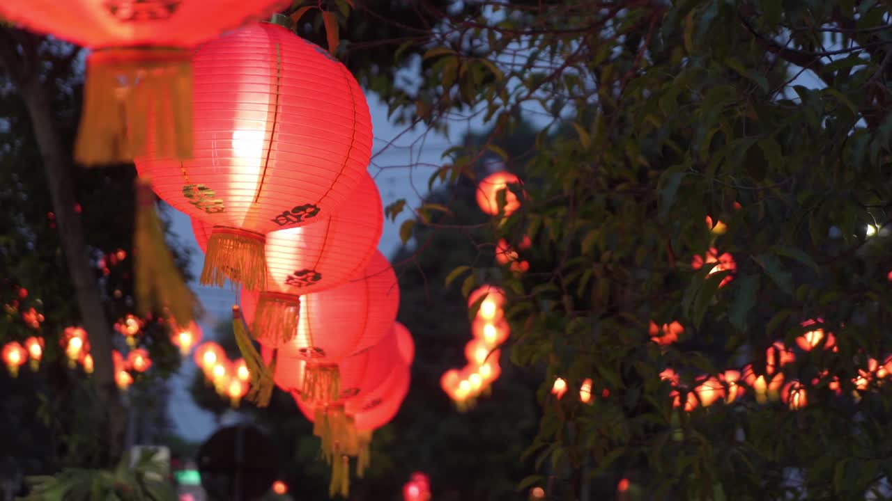 Red Chinese lanterns glowing at dusk during festival, hanging outdoors with trees in background
