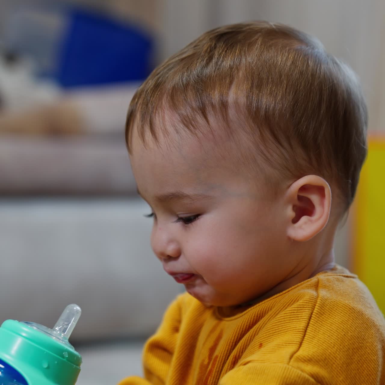 Adorable little Caucasian boy drinking water from bottle. Kid spills the drink and looks carefully at the bottle. Close up. Blurred backdrop