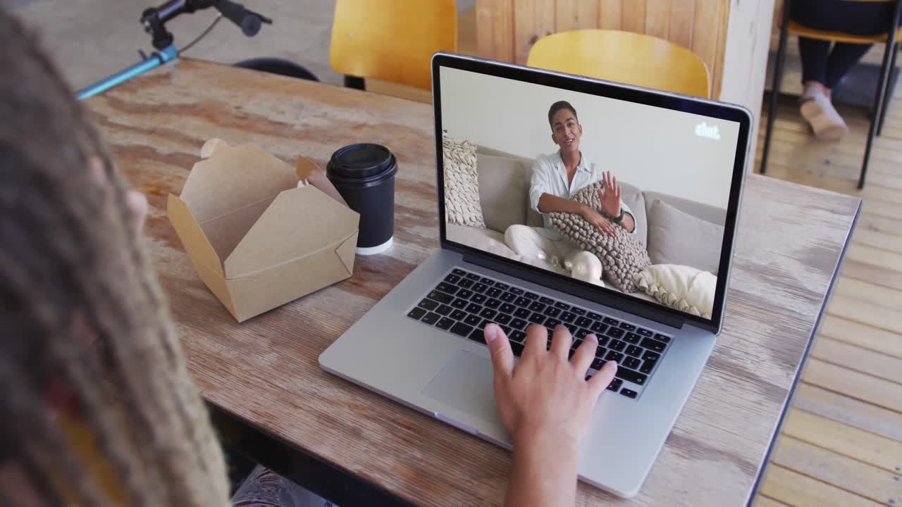 Mixed race man sitting in cafe using laptop making video call with male friend