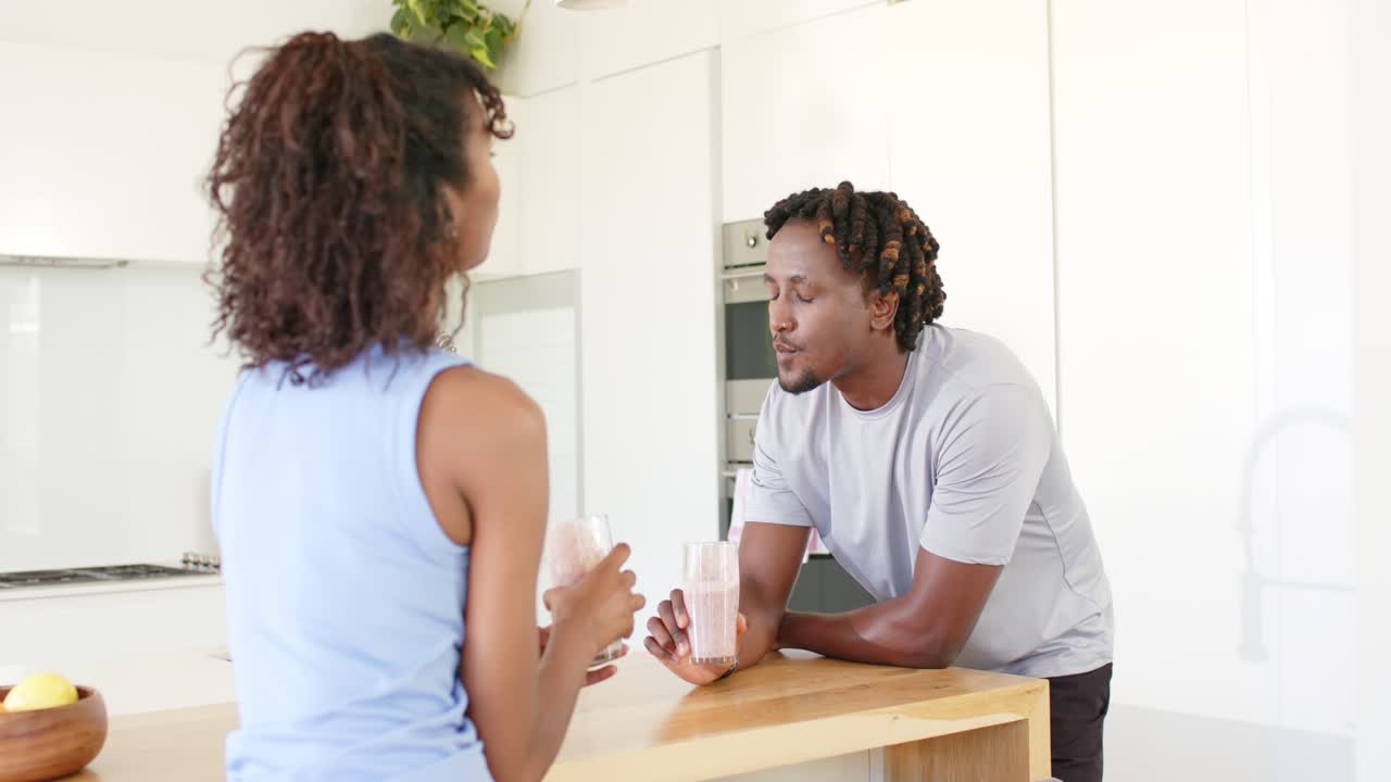 African American couple lifting glasses and tasting pink drinks while talking at wooden island