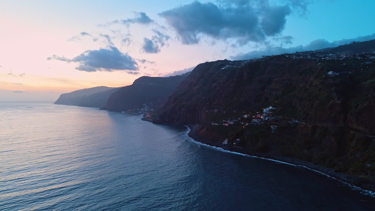 Multiple houses located on the slopes of the high mountains on the shore of the Madeira Islands, Portugal. Twilight view of the rocks at the Atlantic Ocean. Top view.