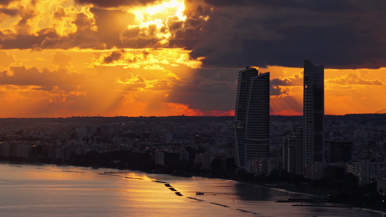 Vista aérea de drone da costa da cidade de Limassol ao pôr do sol com luz dourada quente refletindo no Mar Mediterrâneo.