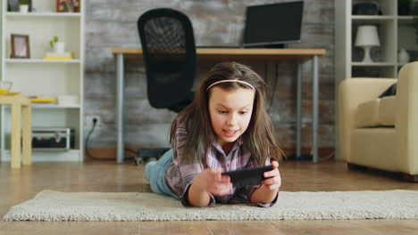 cheerful little girl lying down on the floor playing video games