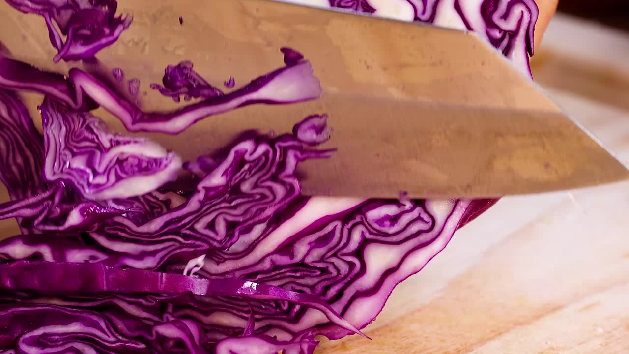 Detailed view of a knife cutting through vibrant purple cabbage layers on a wooden surface.