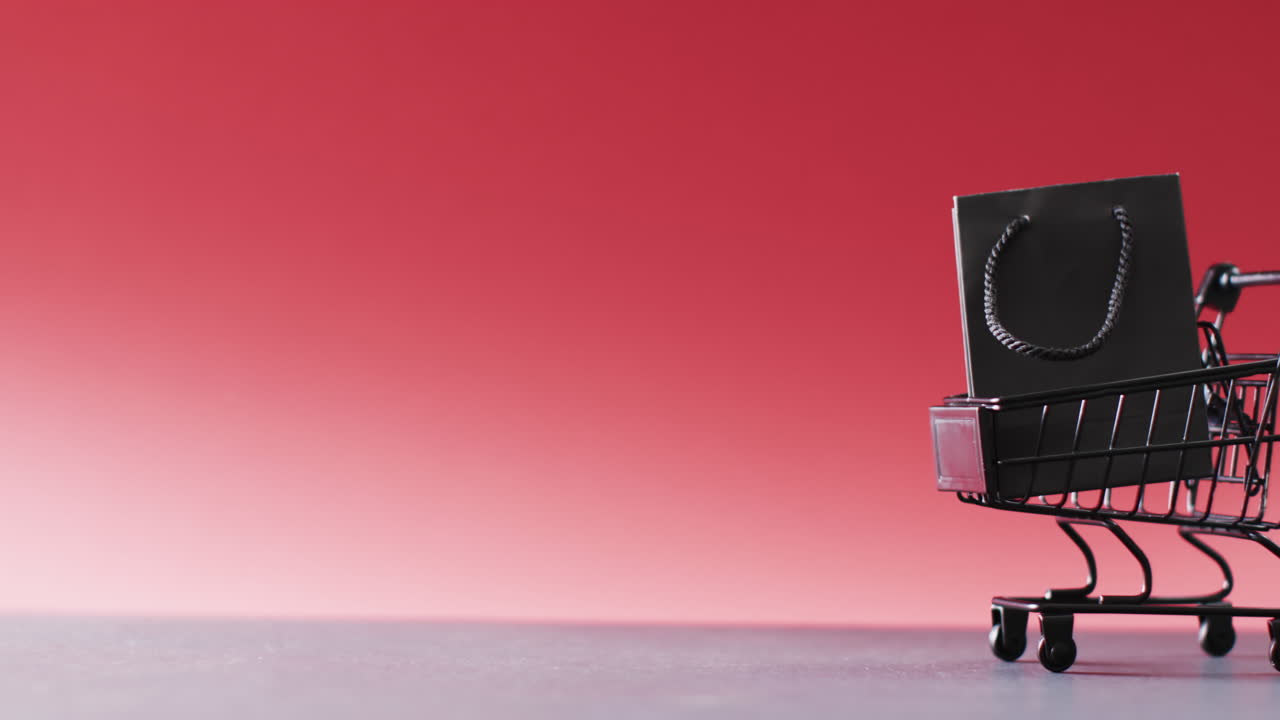 빨간색 배경 에 복사 공간 을 가진 쇼핑 트롤리 에 있는 검은색 선물 가방 의 비디오