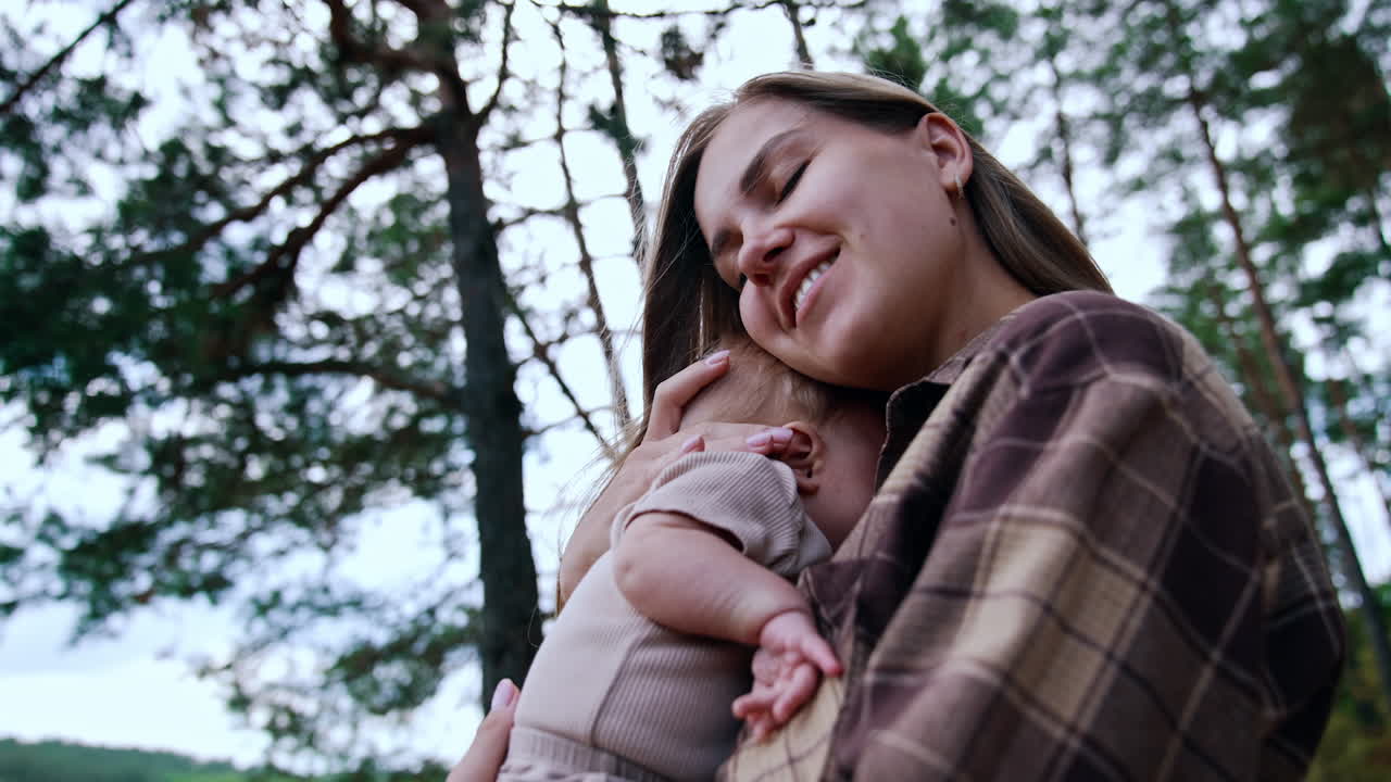 Caucasian mother with her newborn baby in the nature. Woman holds her baby closer to her heart to protect from wind. Low angle view.