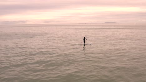 paddle boarder riding alone on calm glowing orange seascape horizon