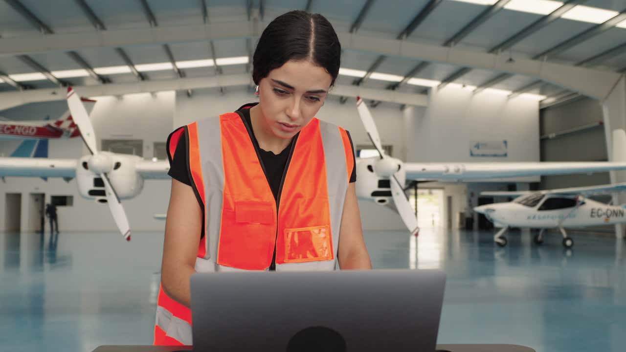 Woman working on laptop in airplane hangar
