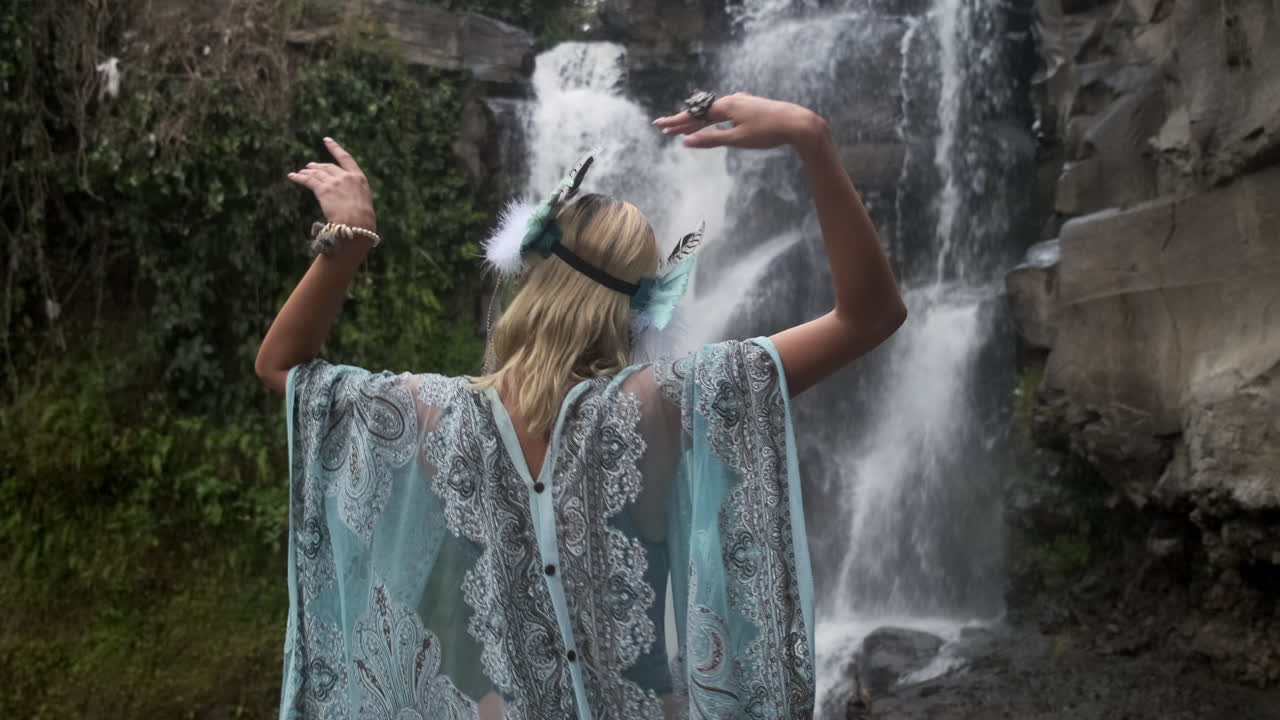 Woman in a Turquoise Dress Posing in Front of a Waterfall