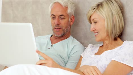 Happy-couple-chatting-and-using-laptop-in-bed