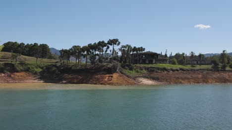 ruined mansion of pablo escobar 'la manuela,' located by lake in colombia, with trees and clear blue sky - view from passing boat