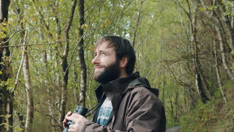 medium shot of male bearded birdwatcher looking up with binoculars in forest in slow motion