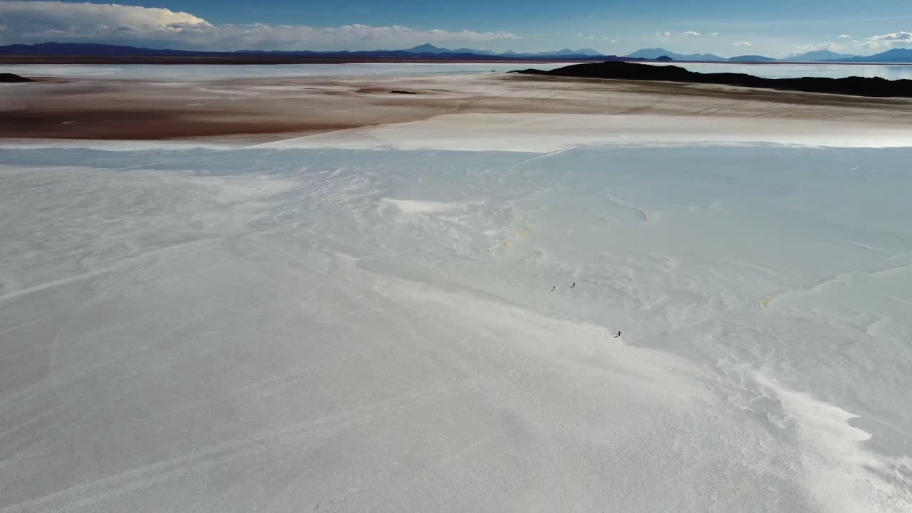 Very tiny people walk on vast salt flat at Uyuni, Bolivia, aerial view