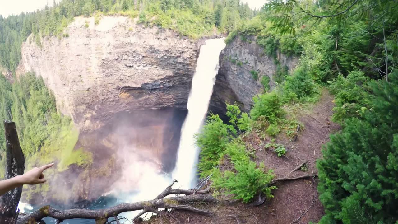 mujer apuntando hacia la cascada en el acantilado 4k